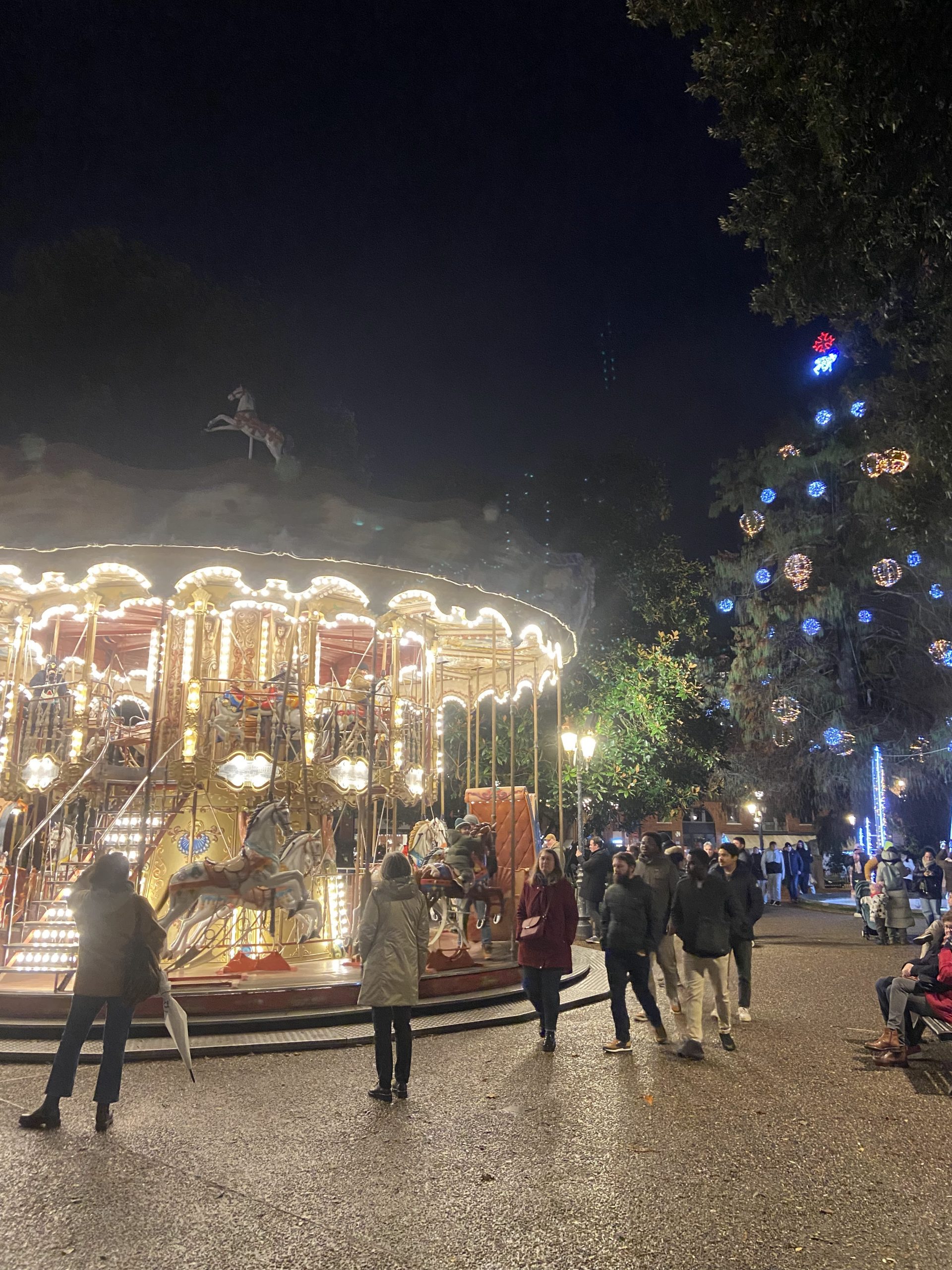 Un carrusel iluminado en un parque, con personas caminando alrededor durante la noche.